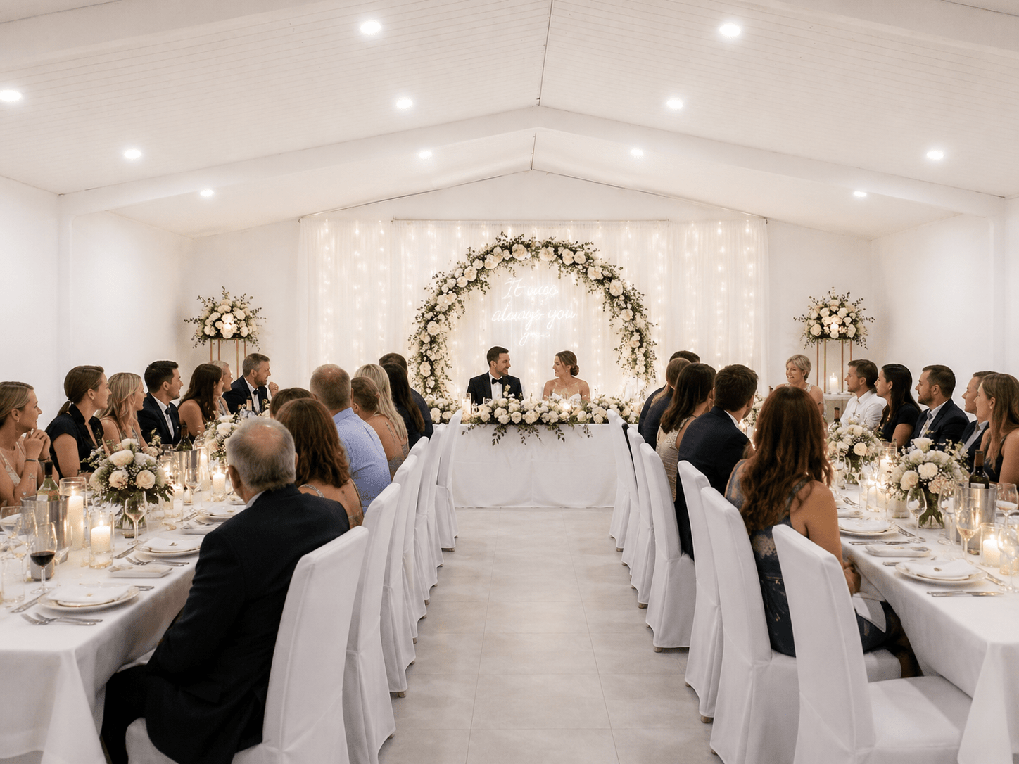 Wedding reception at Berrima Retreat's events room featuring elegant white chair covers, floral decorations, banquet seating, and a romantic bridal table.